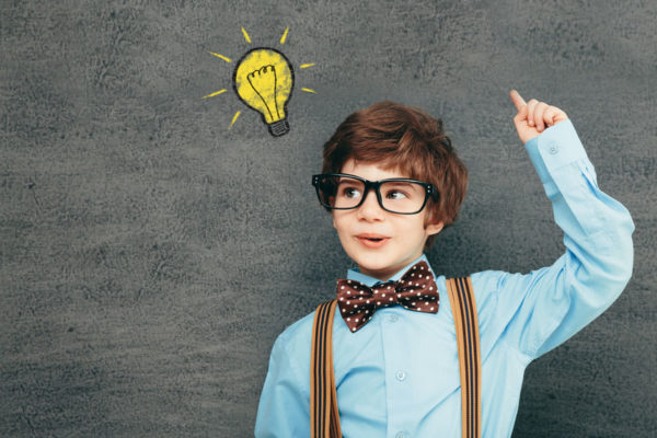 29565168 - cheerful smiling little kid (boy) against  chalkboard; raised his hand up. looking at camera. school concept