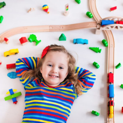 48147283 - child playing with wooden train, rails and cars. toy railroad for kids. educational toys for preschool and kindergarten children. little girl at daycare. view from above, kid playing on the floor.